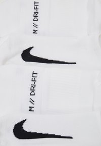 Białe skarpetki z czarnym logo Nike w kształcie łuku oraz napisem "DRI-FIT". Wykonane z teksturowanej tkaniny z żebrowanymi akcentami u góry.
