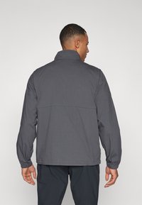 Gray jacket with a high collar, long sleeves, and elastic cuffs. Smooth fabric with a simple design, tailored fit, and minimal detailing.