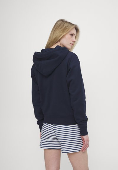 Sweatshirt com capuz azul-marinho, em mistura de algodão e com bainha canelada, combinado com calções listrados em branco e azul-marinho. Vista mostra a parte de trás do conjunto.