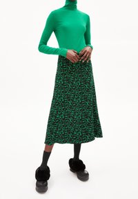 Grön polotröja kombinerad med en midikjol med mörkgrön blommönster. Modellen har på sig fluffiga svarta tofflor och mörka strumpor.