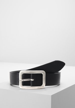 Zwarte lederen riem met een grote rechthoekige zilveren metalen gesp, opgerold weergegeven op een wit oppervlak met een minimalistische achtergrond.