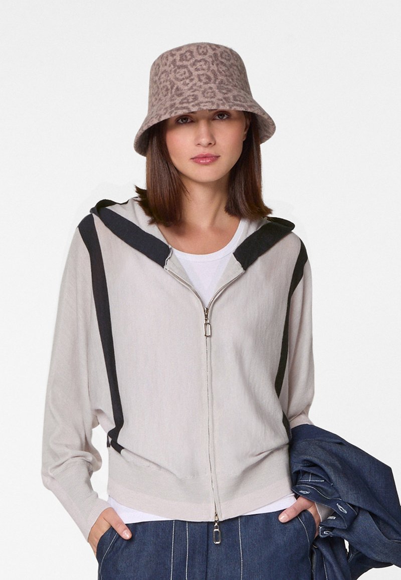 Hellegrauer Reißverschluss-Hoodie mit schwarzen Akzenten, weicher Textur und Kapuze. Kombiniert mit einem beigen Bucket Hat im Leopardenmuster und Jeans.