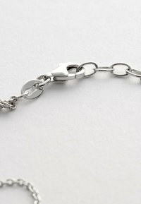 Sølv kædehalssmykke med lås delvist lukket på en hvid overflade, der viser sammenkoblede ovale og cirkulære metalringe.