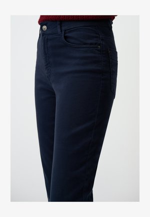 Jeans w kolorze granatowym z mieszanki bawełny o dopasowanym kroju, z bocznymi kieszeniami i guzikiem w przedniej części pasa. Gładka tekstura i minimalne detale przeszyć.