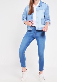 Svetle modrá džínová bunda s ohrnutými rukávy, pod ní bílá košile a tmavě modré úzké džíny. Bílé tenisky dokončují celý outfit.