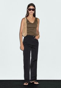 Olive green tank top, black straight-leg jeans, beige bag, and black flip-flops. Accessories include oversized sunglasses and a bracelet.