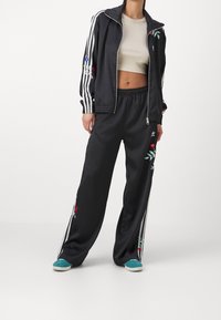 Svart träningsdress med vita ränder; zip-jacka med blommig broderi. LOOSE byxor; teal skor fulländar outfiten.