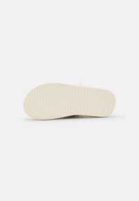 Shoe sole features a textured, wavy design in cream color, with a rounded shape and a smooth finish, showcasing rubber material and durability.