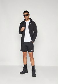 Black outdoor outfit featuring a zippered jacket, t-shirt, and shorts. Accessories include sunglasses and rugged boots for durability.