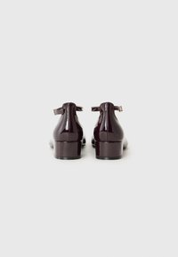 Dunkel glänzende Lackleder-Pumps mit Knöchelriemen, die eine glänzende Oberfläche und einen moderaten Blockabsatz aufweisen, von hinten betrachtet.