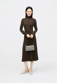 Καφέ ριχτό πλεκτό φόρεμα με μακριά μανίκια και ψηλό λαιμόκοψη, συνδυασμένο με μια τσάντα με σχέδιο και μπεζ slingback ψηλοτάκουνα.