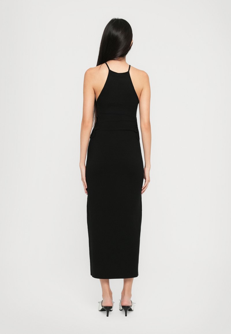 Robe noire sans manches avec un corsage ajusté et une jupe droite, comportant des boutons décoratifs à la taille et une longueur mi-mollet.