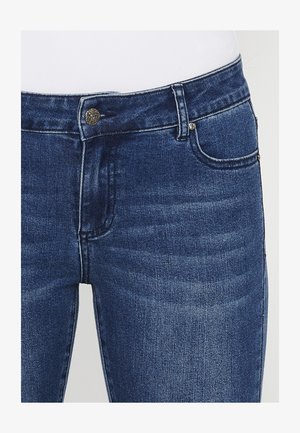 Jeans in denim blu scuro con vestibilità slim, dotati di chiusura con bottone anteriore, cinque tasche e un leggero sbiadimento del tessuto.