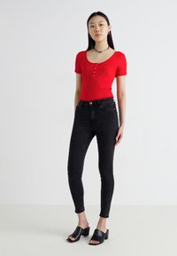 Body vermelho canelado de manga curta com botões, combinado com jeans skinny pretos de cintura alta e mules pretos de salto aberto.