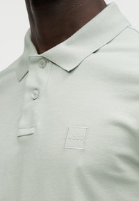Ανοιχτό πράσινο πόλο πουκάμισο με υφή υφάσματος, τρείς κουμπότρυπες και μικρό, λευκό κεντημένο λογότυπο "BOSS" στο στήθος.