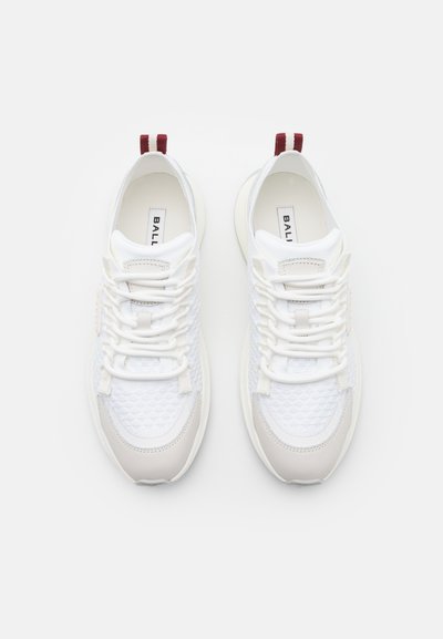 White sneakers with textured mesh upper, smooth leather accents, and a soft outsole. Features red and white pull tabs at the back.