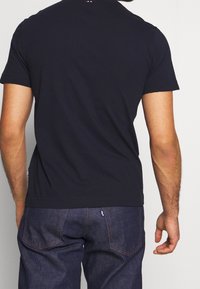 Marinblå bomullströja med korta ärmar, rundad halsdesign, slät textur, med en liten broderad logotyp vid baksidan av halsringningen.