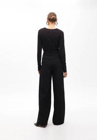 Zwarte lange mouw top met een ronde hals, gecombineerd met hoge taille, wijde zwarte broek. Bevat een klein gouden logo op de achterkant.