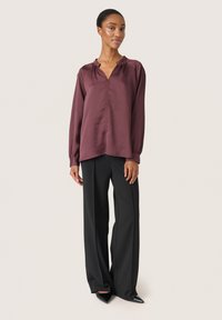 Burgundy blus med långa ärmar har en V-ringning och rynkade axlar, i kombination med svarta skräddarsydda byxor och spetsiga svarta klackar.