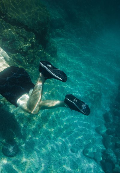 Chaussures de sport noires avec accents blancs immergées sous l'eau, présentant une semelle en caoutchouc texturée, un matériau supérieur lisse et un design minimaliste.
