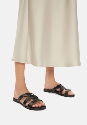 Czarne skórzane klapki na płaskiej podeszwie z wieloma krzyżującymi się paskami i ozdobnym srebrnym elementem. Płaska podeszwa o gładkiej fakturze.