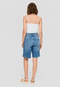 Blaue Jeansshorts mit lockerer Passform, ausgefranstem Saum und vier Taschen. Kombiniert mit einem weißen Tanktop und hellen Sandalen.