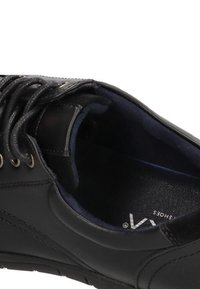 Zapatilla negra de cuero con punta redonda, superficie texturizada, diseño de cordones y interior acolchado. Presenta una sutil marca en el interior.