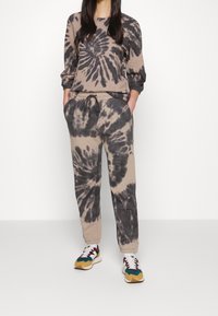 Tie-dye loungewear-set i beige och mörkgrått. Toppen har långa ärmar och rund hals; byxorna har resårmidja och fickor.