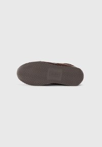 Brown shoe sole with a herringbone pattern, featuring a rectangular embossed logo. Texture is rubber with a slight sheen and sturdy design.