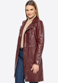 Cappotto in pelle bordeaux con un design aderente, chiusura con zip e tasche laterali. Caratterizzato da una texture liscia e un colletto classico.