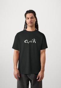 Svart bomulls t-shirt med kort ärm, med en stiliserad vit logotyp "Quik" på framsidan. Enkel design med avslappnad passform.