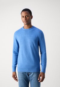 Hellblaues Sweater aus weichem, strukturiertem Stoff. Verfügt über einen runden Halsausschnitt sowie gerippte Bündchen und Saum. Getragen über blauen Jeans.