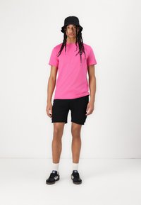 Lyserød bomulds-t-shirt, sorte cargo-shorts, sorte bøttehat og sorte sneakers med hvide striber; enkel design, minimal detaljer.