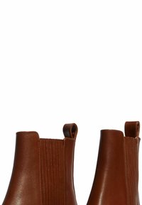 Botas de nivel tobillo de cuero marrón con paneles elásticos acanalados, diseño de punta redondeada y tiradores para poner y quitar fácilmente. Textura suave sin patrones visibles.