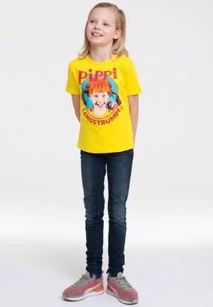 Yellow t-shirt with a graphic print of a girl with red hair, dark jeans, and pink-accented sneakers.