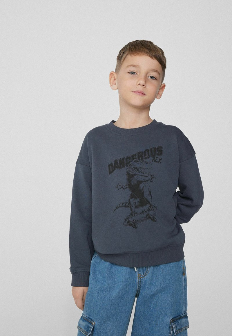 Tmavě modrý svetr s kulatým výstřihem, zdobený černou grafikou dinosaura a textem "DANGEROUS REX". Měkký materiál a volný střih.