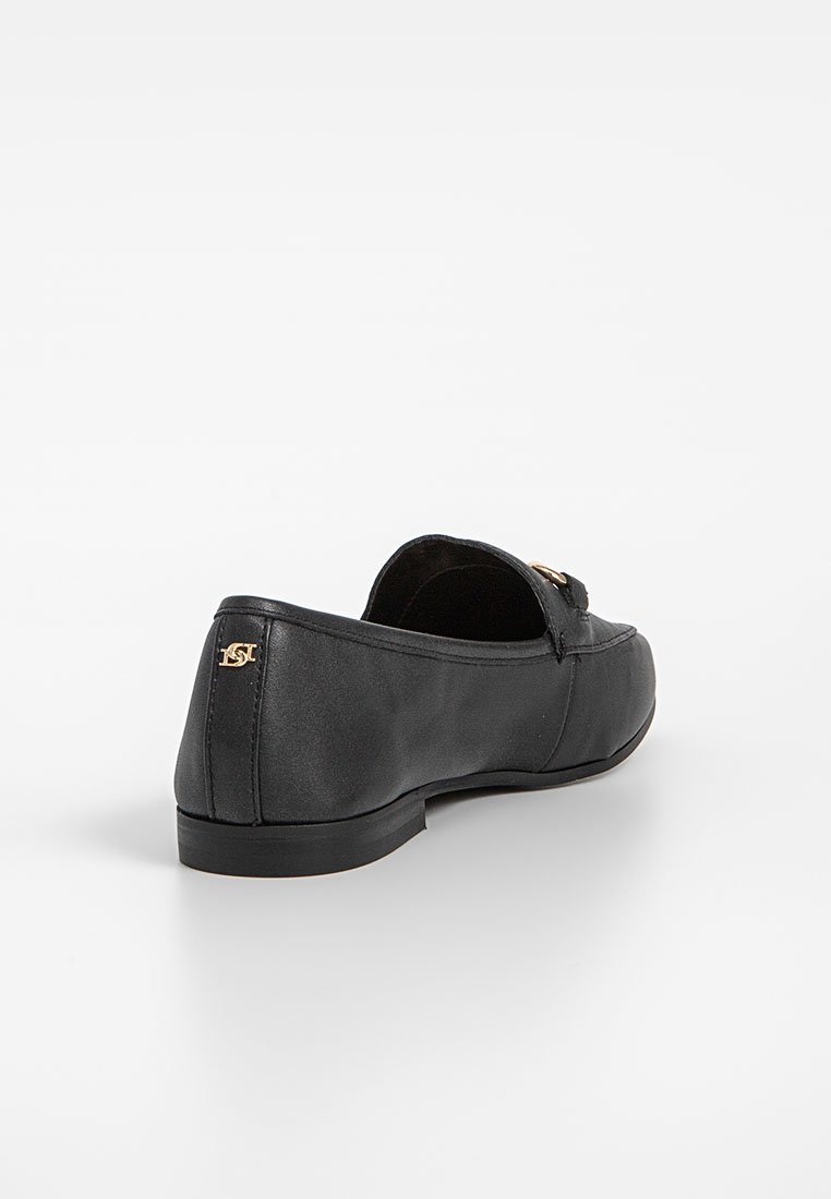 Mocasines de cuero negro con un tacón bajo, que presentan un acento del logo en tono dorado en el costado y una textura suave y pulida.