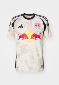 Krátký rukáv, béžový fotbalový dres s černými akcenty, digitální maskáčový vzor a logo Red Bull umístěné uprostřed na přední straně.