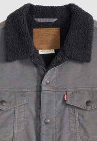 Γκρι μπουφάν Levi's με μαύρο γιακά sherpa, μεταλλικά κουμπιά, δύο τσέπες στο στήθος και εμφανές κόκκινο ετικέτα Levi's στην αριστερή τσέπη.