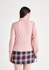 Blush pink pleated blouse with long sleeves and a collar. Paired with a black and plaid skirt featuring blue, red, and gray lines.