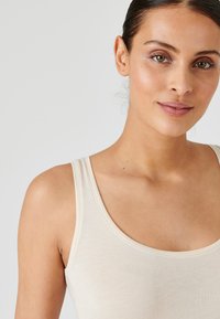 Beige tanktop met dunne schouderbandjes, een ronde halslijn en een zachte, gladde textuur. Eenvoudig ontwerp zonder zichtbare patronen of accenten.