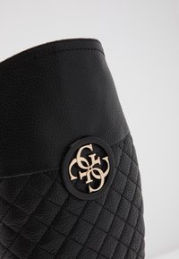 Mustahdara mweusi ya ngozi yenye muundo wa quilt, ikionyesha alama ya dhahabu kubwa na kingo ya juu ya laini ya mweusi.