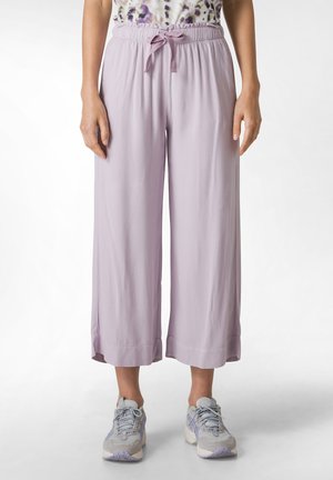 Pantaloni larghi di colore viola chiaro realizzati in materiale morbido, con cintura elastica e coulisse. Abbinati a sneakers grigie e viola.