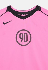 Ροζ αθλητική φανέλα με μαύρο γιακά, μαύρο λογότυπο Nike στο αριστερό στήθος και αριθμός 90 μέσα σε μαύρο κύκλο στο κέντρο εμπρός.