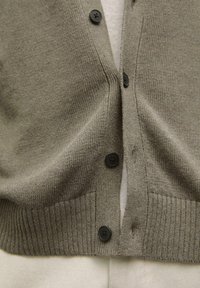 Grauer gestrickter Cardigan mit V-Ausschnitt, ausgestattet mit schwarzen Knöpfen und geripptem Saum. Zwei seitliche Taschen mit einer weichen Textur.