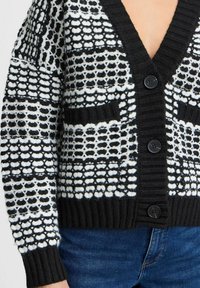 Melnbalts adīts kardigāns ar V-veida kakla izgriezumu, ar teksturētiem rakstiem, ribotām aprocēm un trim pogām priekšpusē.