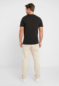 Black short-sleeve t-shirt worn with beige chinos and white sneakers. The shirt features a simple design and a round neckline.