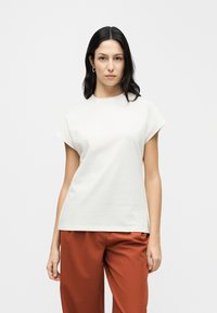 Άσπρο βαμβακερό t-shirt με κοντά μανίκια και στρογγυλή λαιμόκοψη, συνδυασμένο με χαλαρά παντελόνια σε χρώμα σκουριάς. Απλός σχεδιασμός, λεία υφή.