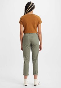 Brun kortärmad t-shirt i kombination med olivgrön byxor med uppvikta ärmar och vita höga sneakers. Mjuk tygkvalitet, avslappnad passform och enkel design.