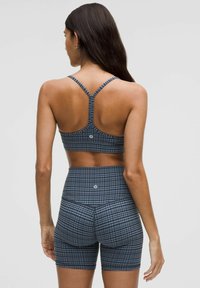 Sujetador deportivo y pantalones cortos de talle alto en azul marino con un patrón de cuadros. Presenta tirantes ajustables y un detalle de logo en los pantalones cortos. Textura suave.